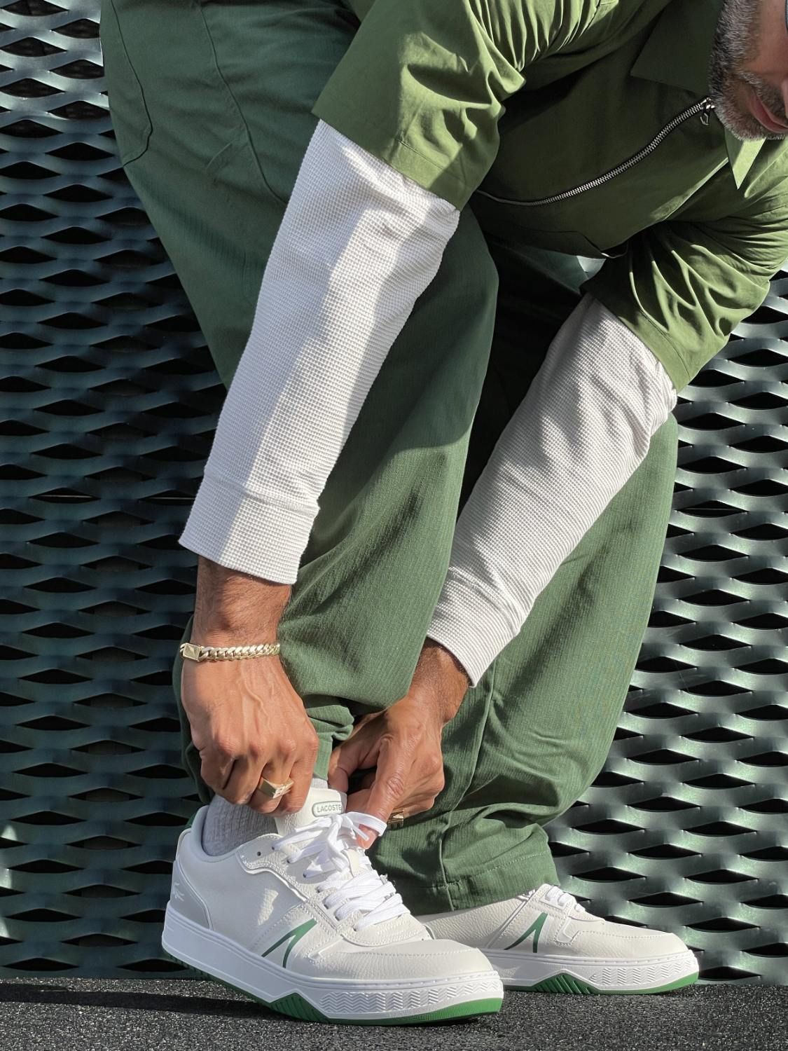 Mads Emil Møller ties his shoelaces, wearing a green outfit and white sneakers.