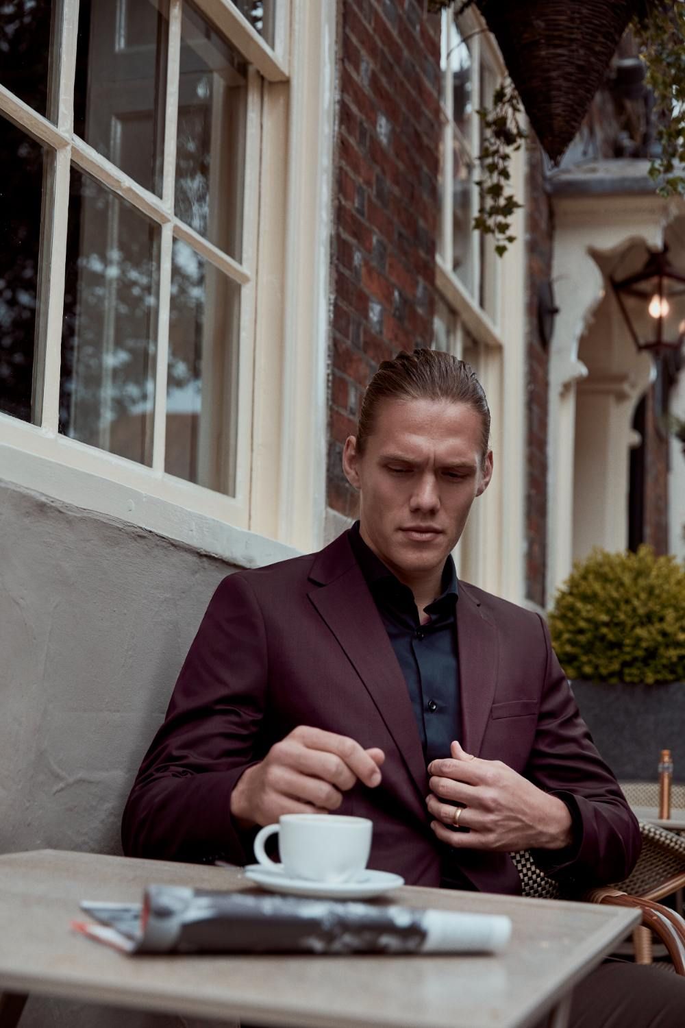 Jannik Vestergaard seated at a café table, adjusting his suit, with a coffee cup nearby.