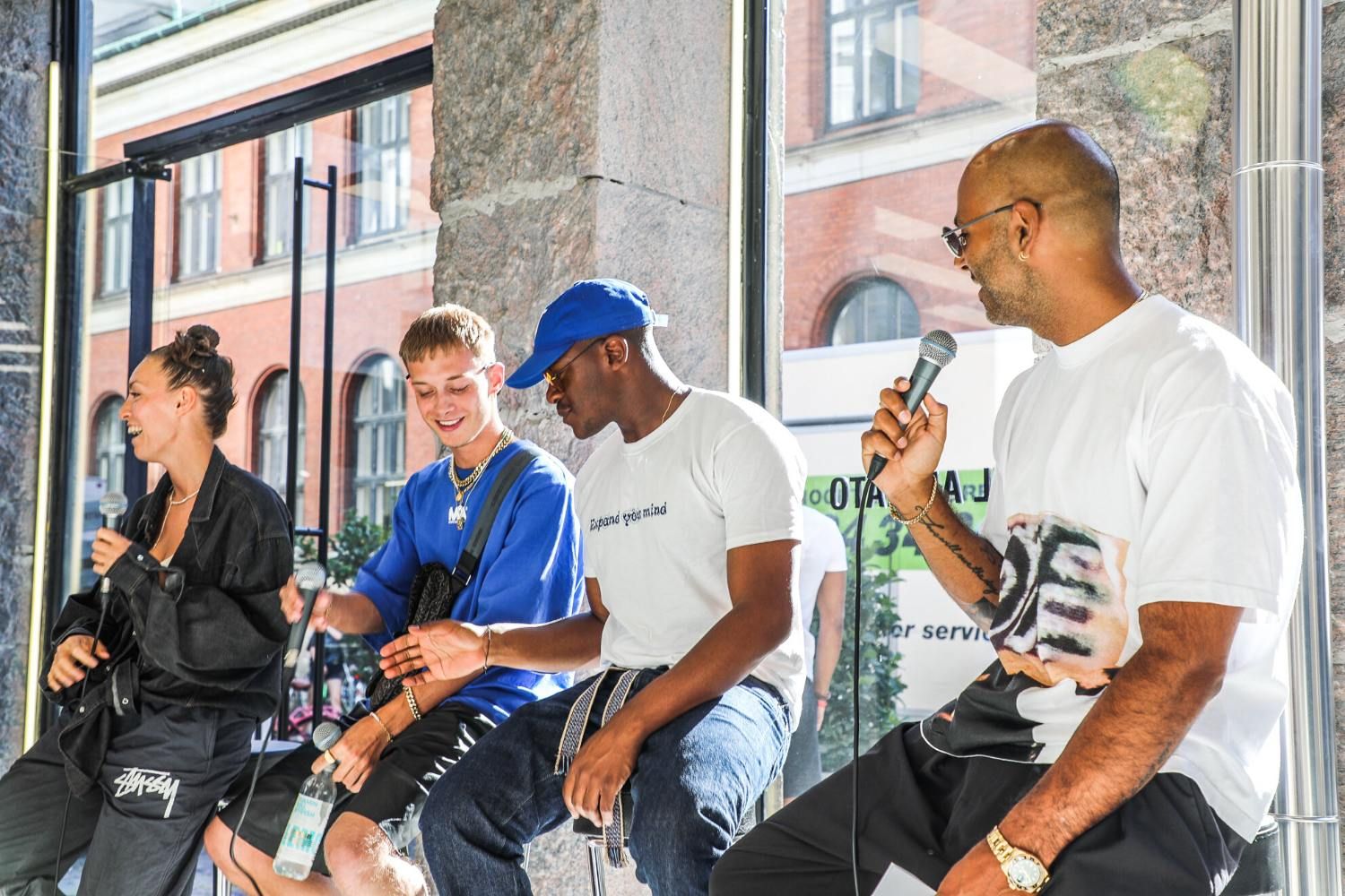 Four individuals seated in a bright, modern space, engaging in conversation with microphones.