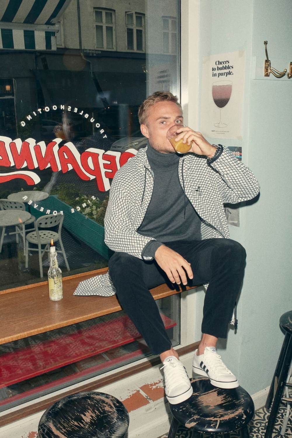 Man sitting on a bar stool, sipping a drink, with a window view and casual atmosphere.