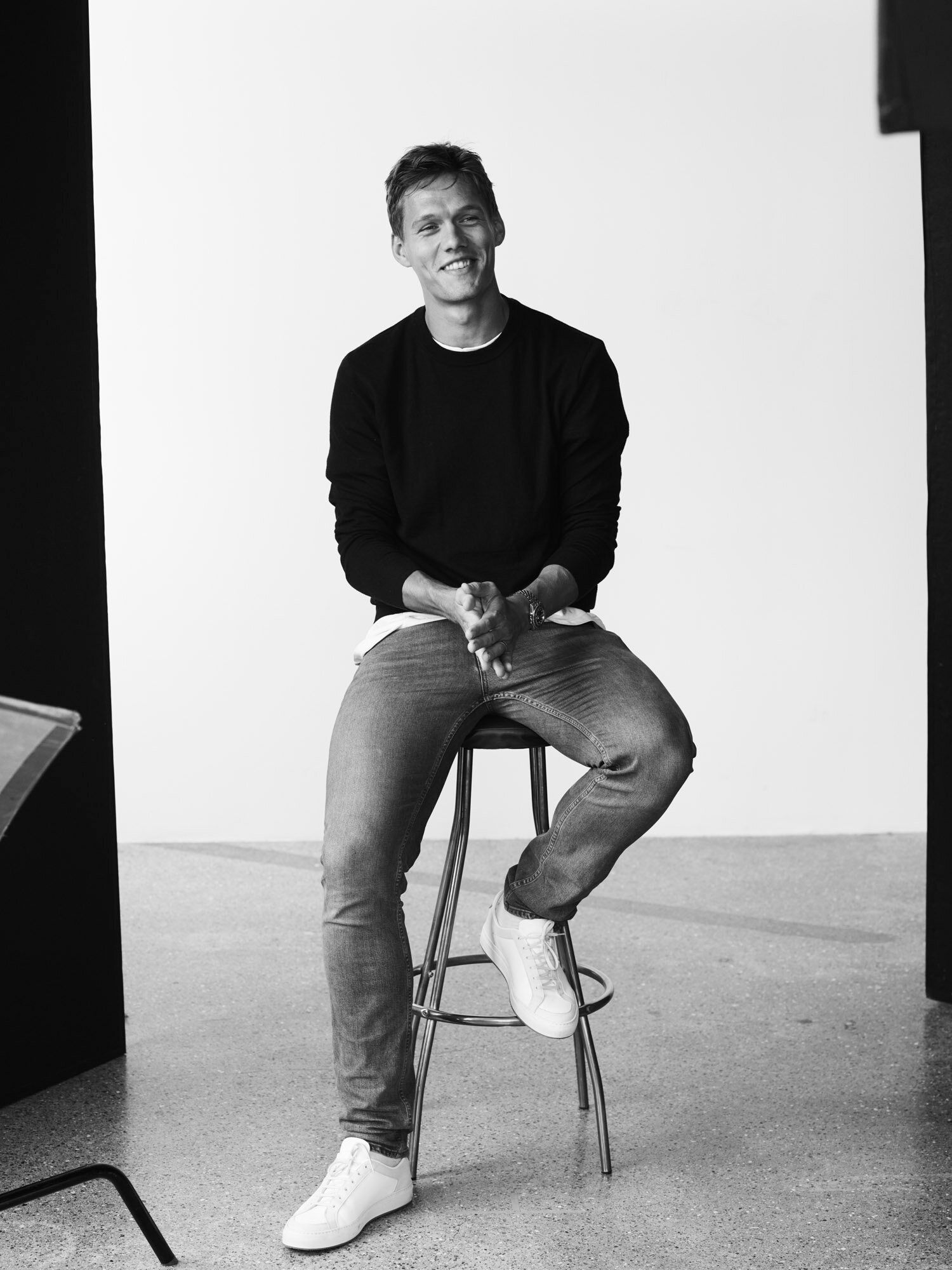 Jannik Vestergaard seated on a stool, smiling in a minimalist studio setting.