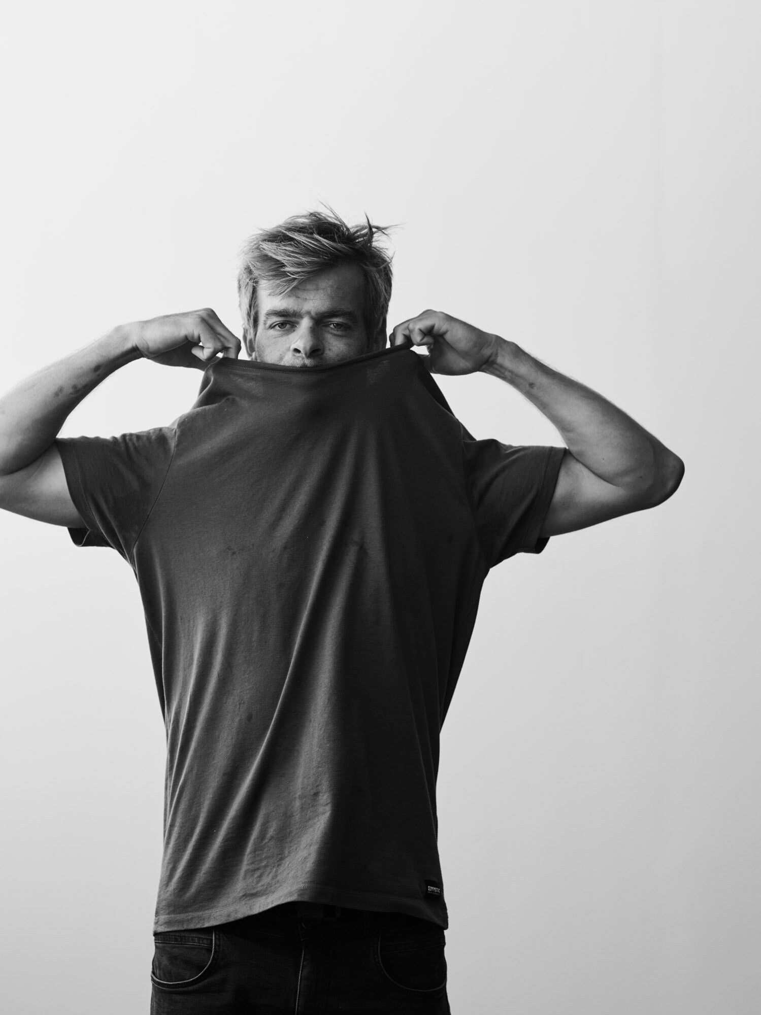 A man pulls a t-shirt over his face against a plain background.
