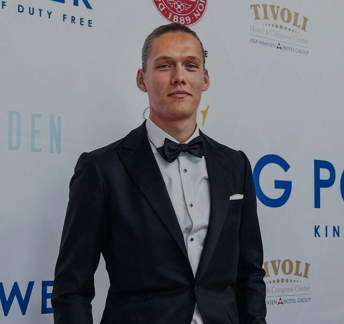 Jannik Vestergaard in a tuxedo, standing confidently against a branded backdrop at an event.