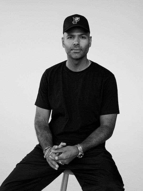 Mads Emil Møller seated, wearing a black shirt and cap, against a neutral background.