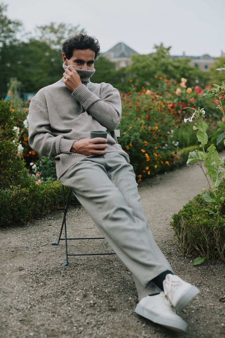 Jonathan Harboe seated in a garden, wearing a gray outfit and holding a cup.
