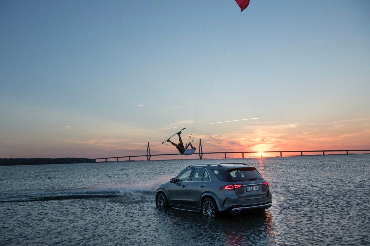 Kiteboarder soaring above water at sunset, with a car partially submerged nearby.
