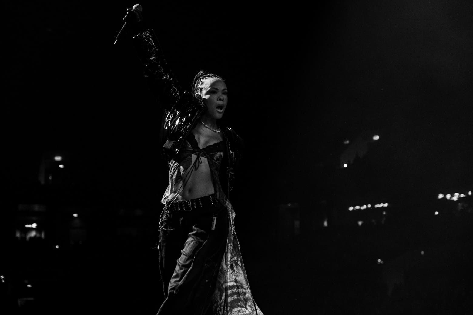 Bathsheba performs energetically on stage, holding a microphone, in a dramatic black and white setting.