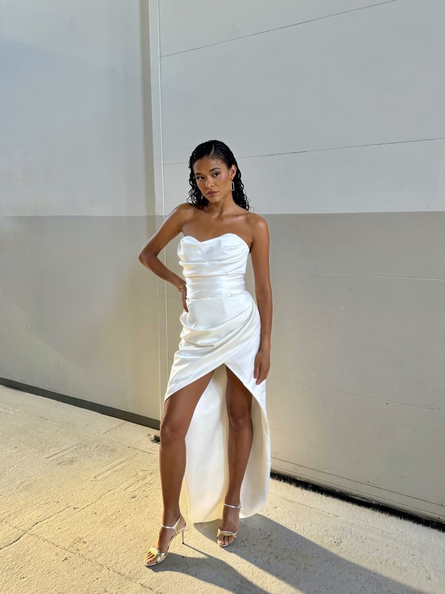 Cilia Trappaud poses in a white dress with a high slit against a neutral background.