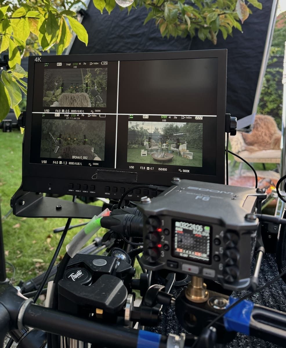 Monitor displaying multiple camera feeds on a film set surrounded by greenery.